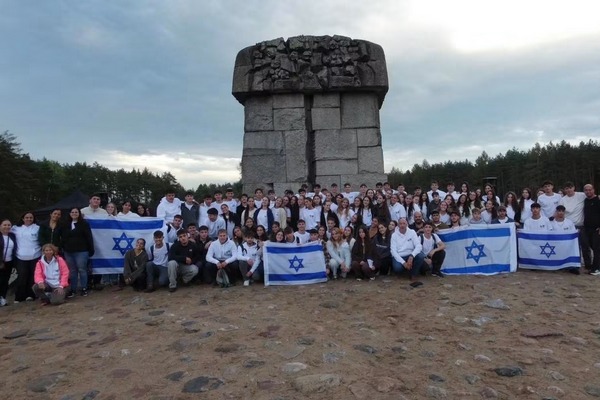 תמונה קבוצתית של משתתפי מסע כיתות יב לפולין עם דגלי ישראל