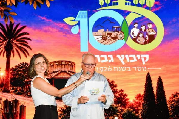 נציג ונציגה עומדים על הבמה במהלך חגיגות המאה לקיבוץ גבת